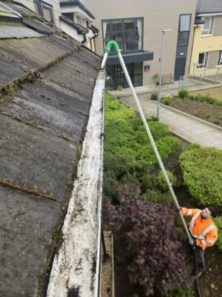 Rope access worker cleaning gutters along a roofline